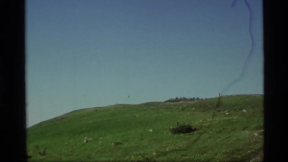 The final 1977 Alaska frame shows a grassy hillside and open blue sky, with a very small figure or marker near the ridge line.
