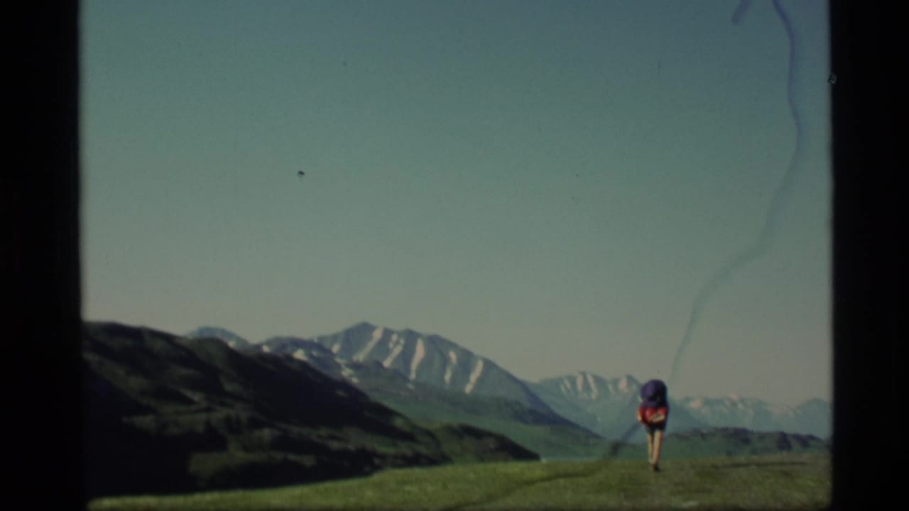Distant backpacker walking on a grassy ridge with snow-capped mountains beyond.