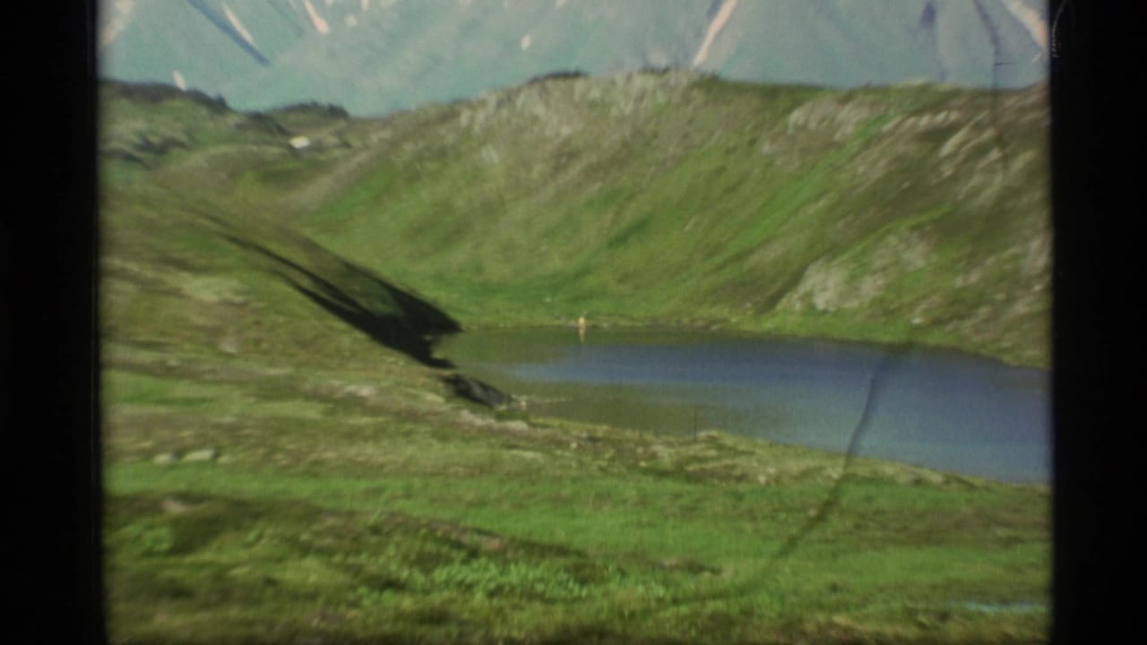 Mountain lake and green valley with snow-streaked peaks in the background.