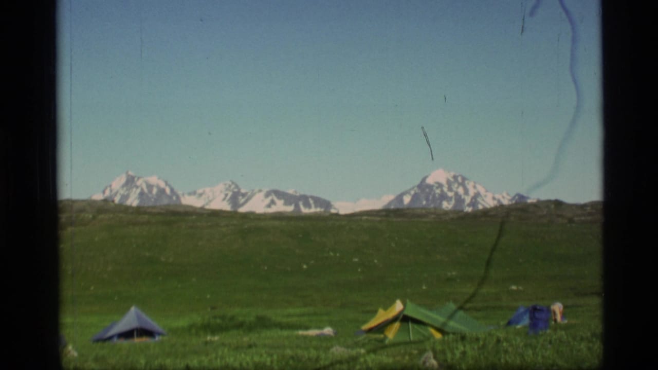 Color tents in a green meadow below distant snow-capped mountains.
