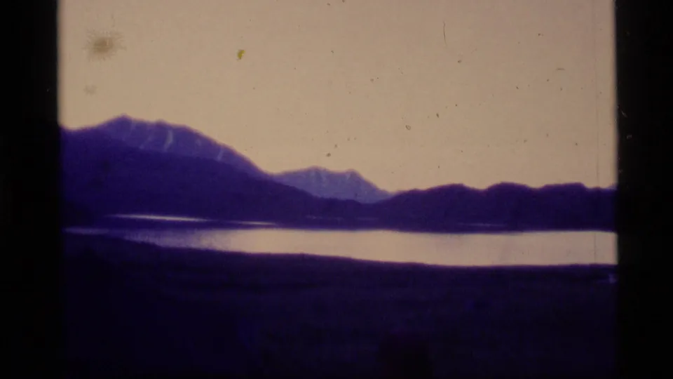 1977 Alaska 8mm frame showing a purple dusk lake with layered mountain silhouettes and heavy film border.
