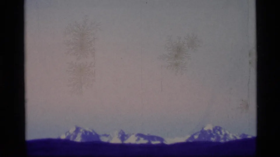 1977 Alaska 8mm frame with distant snow-covered peaks on a dark horizon, pale sky, visible dust, scratches, and purple-blue color shift.