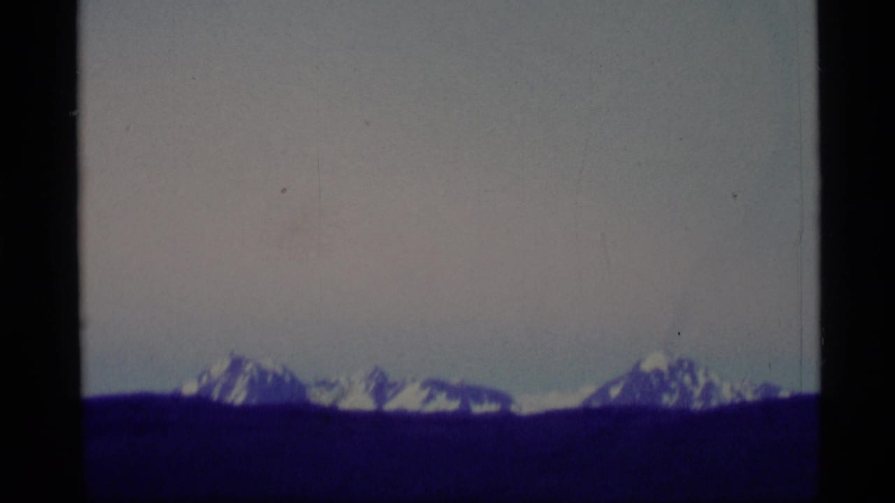 1977 Alaska 8mm frame showing snow-capped mountains across a wide dark field, with visible film gate edges and soft color shift.