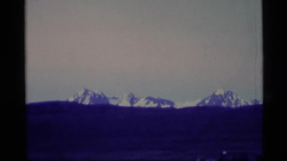 1977 Alaska 8mm frame of distant snowy peaks and a wide open foreground, tinted blue-purple by aged film color.