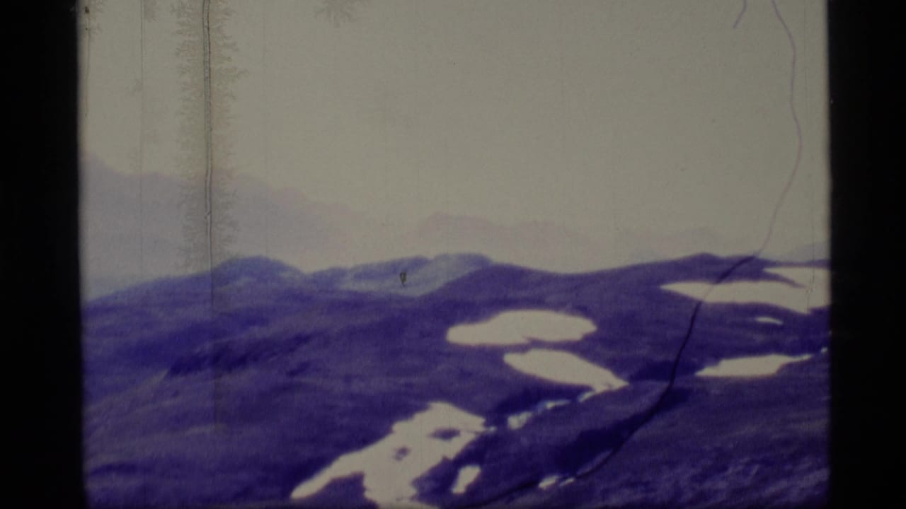 Snow-patched mountain ridges beneath a pale sky, framed by dark 8mm film borders.