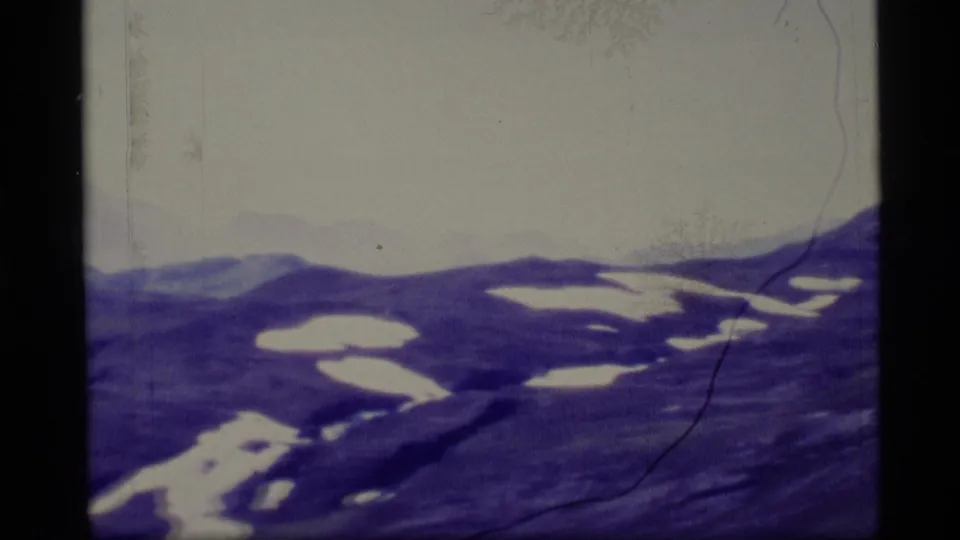 1977 Alaska 8mm view of a broad ridgeline with scattered snowfields, pale sky, soft focus, and physical film scratches.