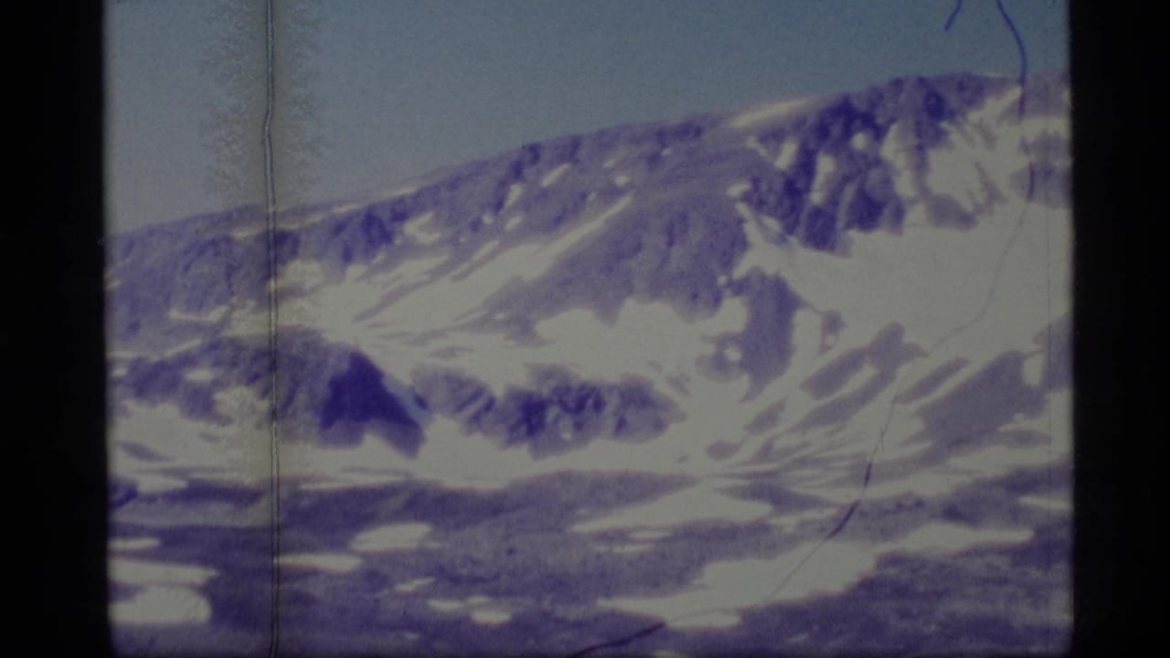 Snow-capped mountain slope beneath pale blue sky with visible 8mm frame edges.