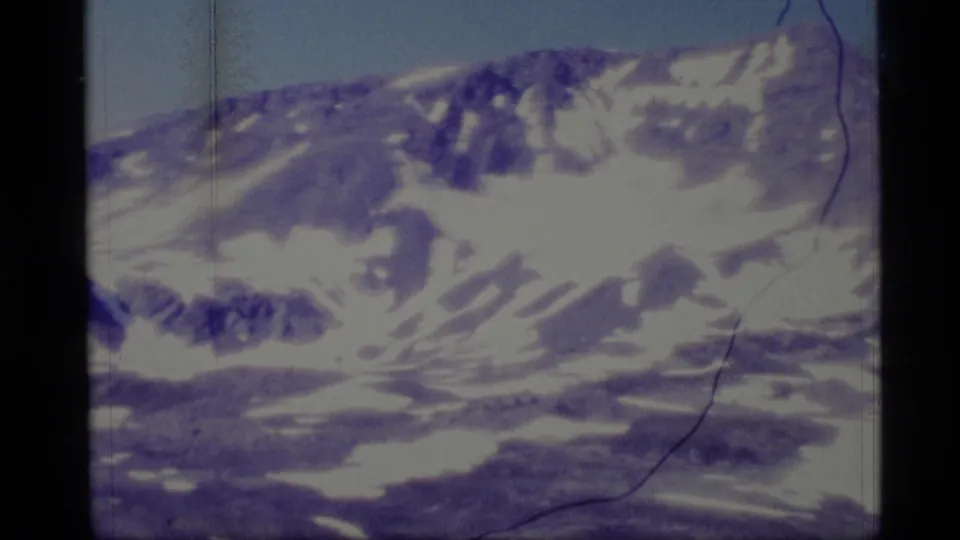 1977 Alaska 8mm view of a wide mountain ridge with snow patches, exposed rock, pale sky, and scanned film scratches along the frame.