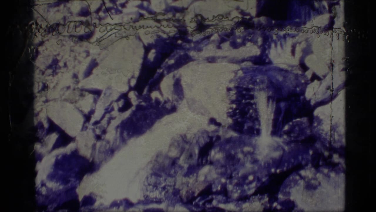 1977 Alaska 8mm frame showing a rocky stream area with pale snow patches, dark boulders, and heavy blue-white film coloration.