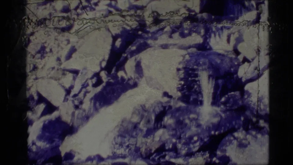 1977 Alaska 8mm frame showing a rocky stream area with pale snow patches, dark boulders, and heavy blue-white film coloration.