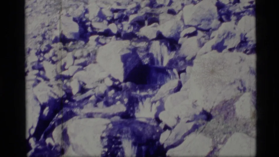 1977 Alaska 8mm frame showing a small cascade among boulders and snow, with soft exposure and handheld home-movie texture.