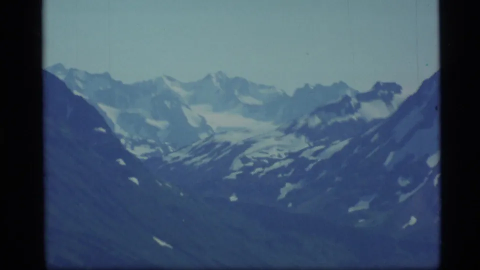 1977 Alaska 8mm view of rugged snow-covered peaks, with cool color shift and visible film gate edges.