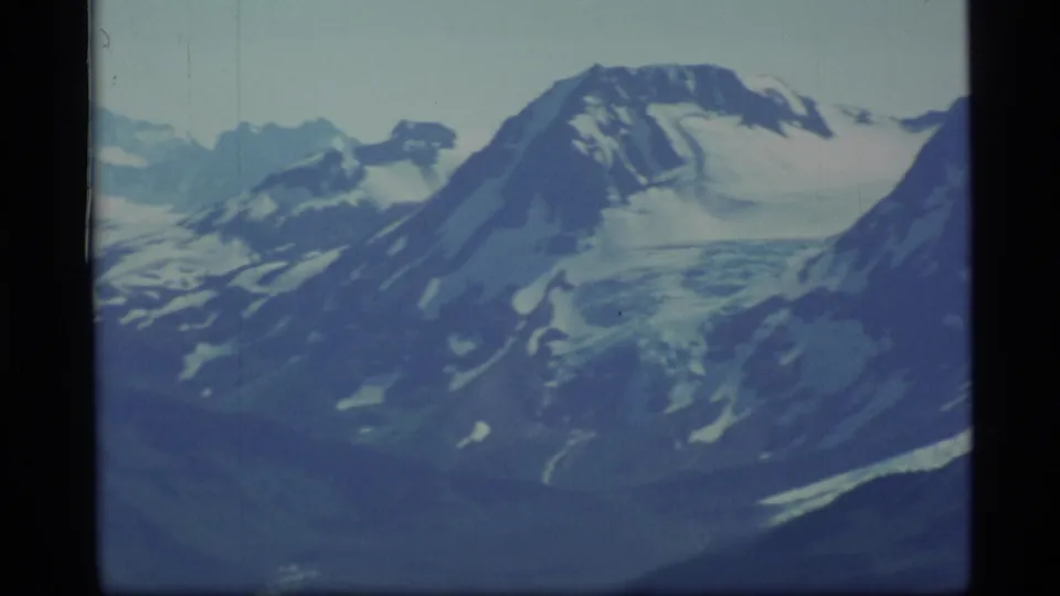 1977 Alaska 8mm frame showing a broad snowfield on a mountain slope with distant peaks behind it.