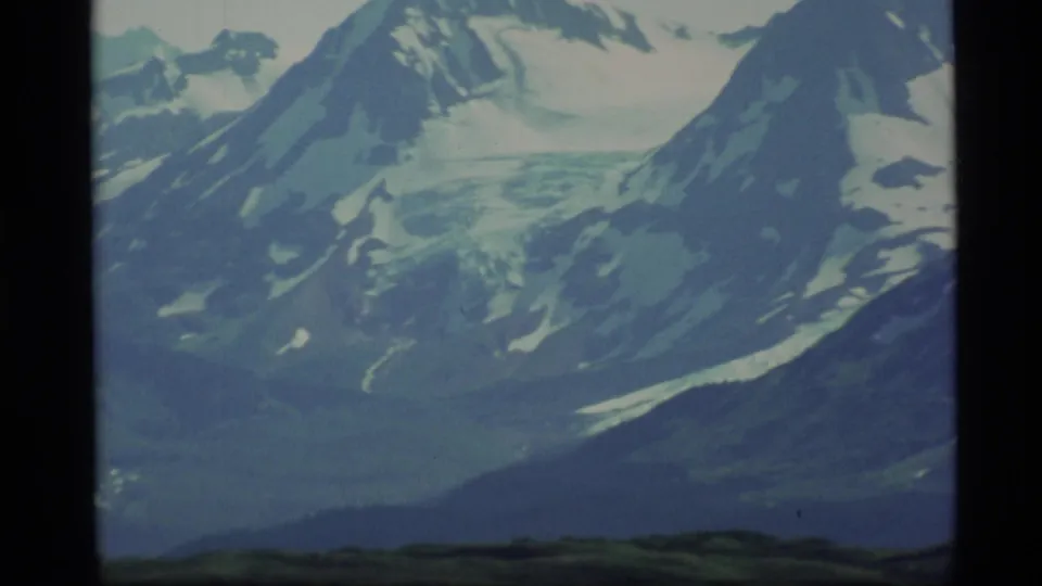 1977 Alaska 8mm frame with a snowy mountain face, glacier-like ice, and low dark hills at the bottom edge.