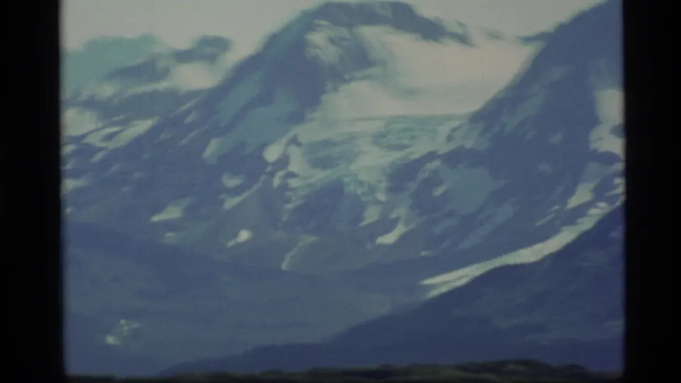1977 Alaska home-movie frame ending on soft snowy peaks, ice fields, and dark slopes in cool aged-film color.