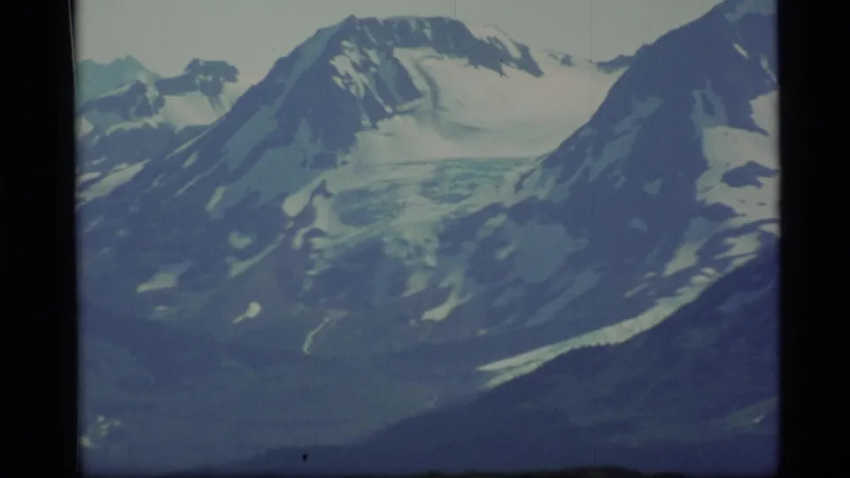 Vintage Alaska travel frame with a snow-streaked mountain range, central ice field, and dark lower terrain.