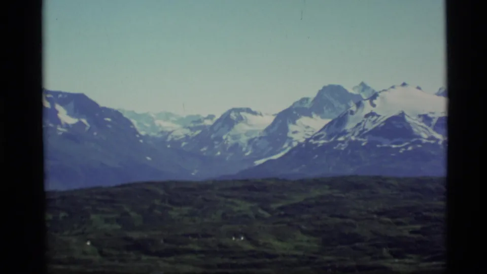 1977 Alaska 8mm frame showing distant snow-covered summits beyond a shadowed tundra-like foreground.