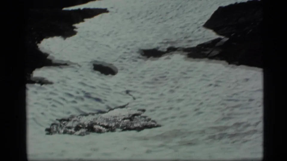 Close 1977 Alaska 8mm view of rippled snow or ice around dark exposed rocks, suggesting spring melt in mountain terrain.