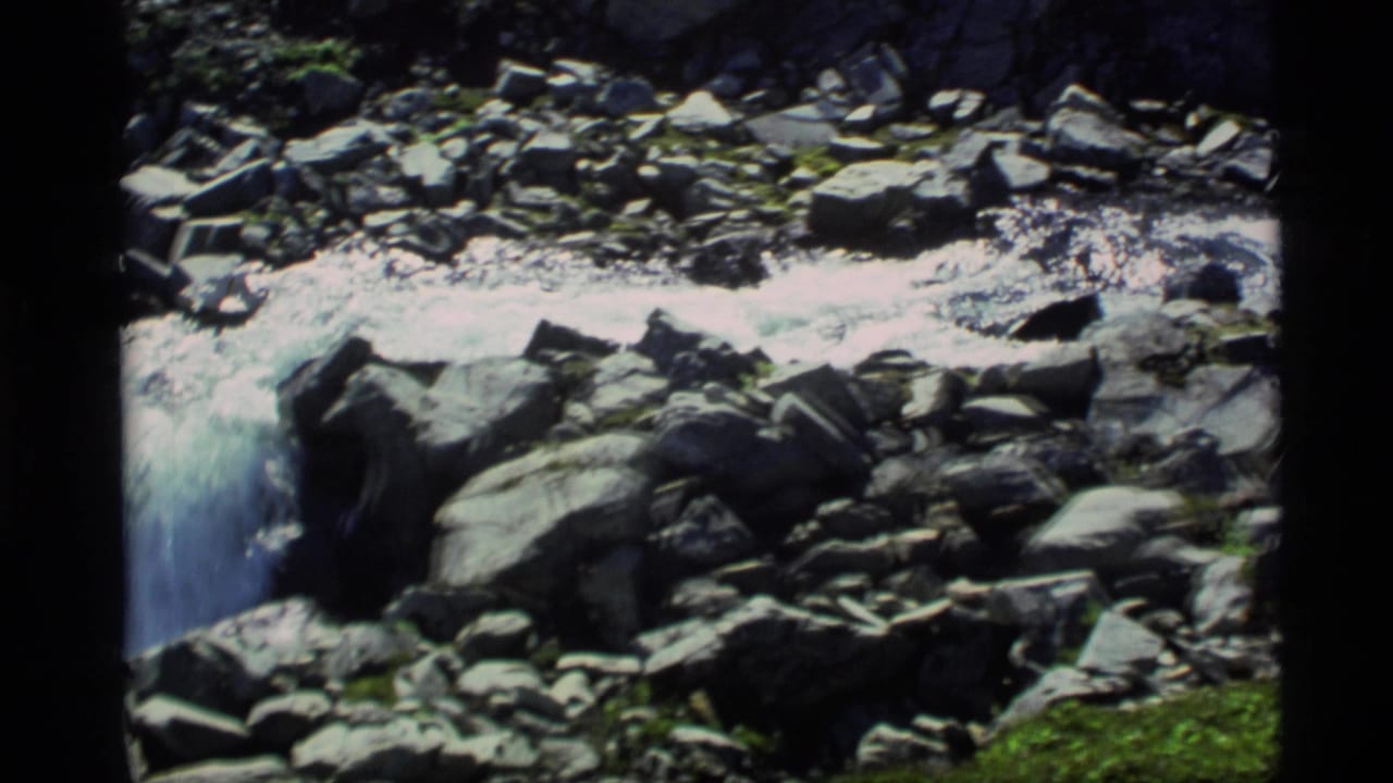 1977 Alaska 8mm frame of water rushing through a rocky streambed with bright foam and moss-covered stones.
