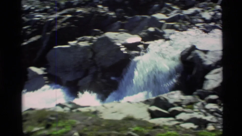 Vintage 8mm Alaska frame showing a short cascade pouring over gray boulders into whitewater.