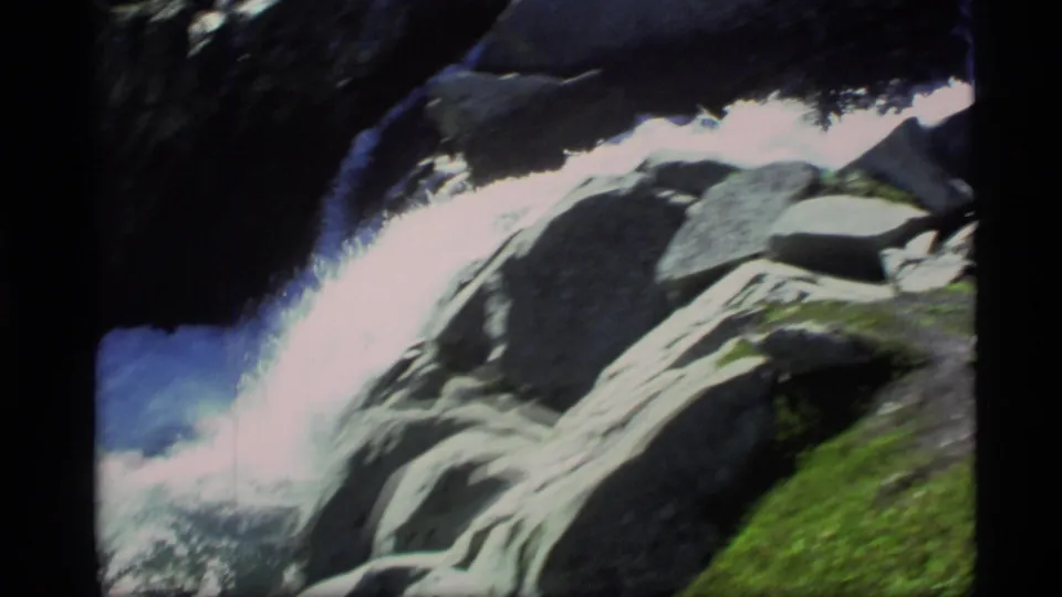 1977 Alaska 8mm frame showing bright whitewater flowing through dark rocks with mossy green banks.