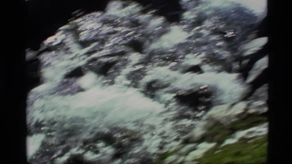 1977 Alaska home-movie frame with foamy water moving through a rocky mountain stream channel.