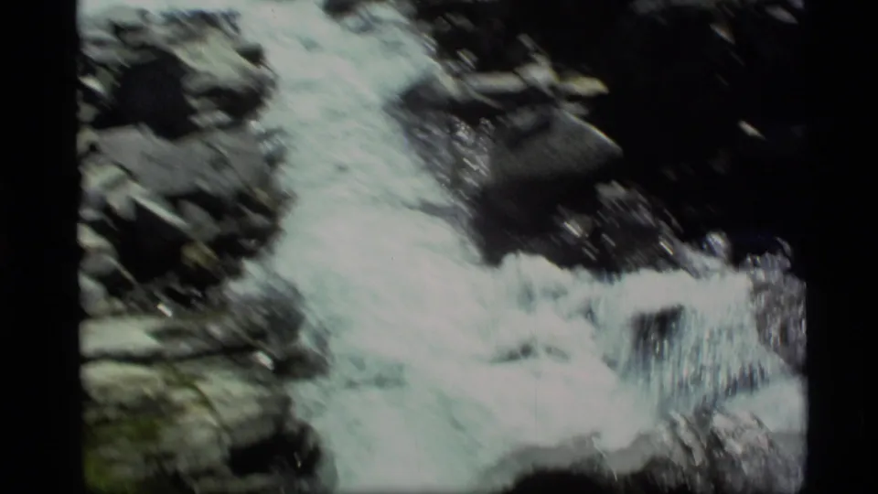 Close 8mm view of Alaska stream rapids, with white water spilling across dark rocks.