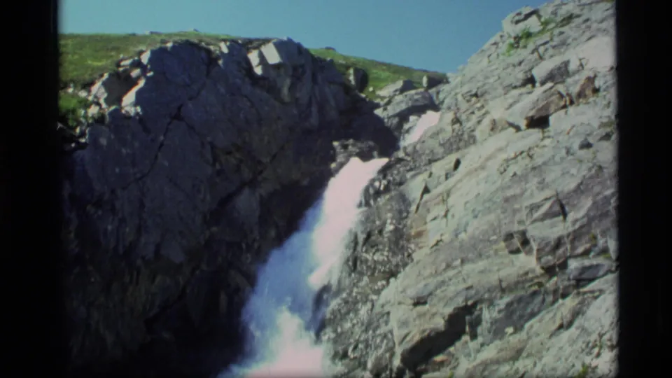 1977 Alaska 8mm frame of turbulent whitewater descending between steep gray rock faces in sun.