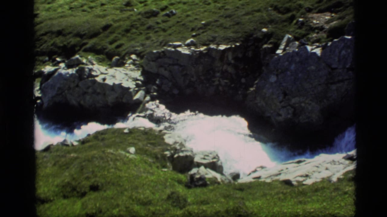 1977 Alaska 8mm frame showing white water moving through dark rocks and green mossy banks.