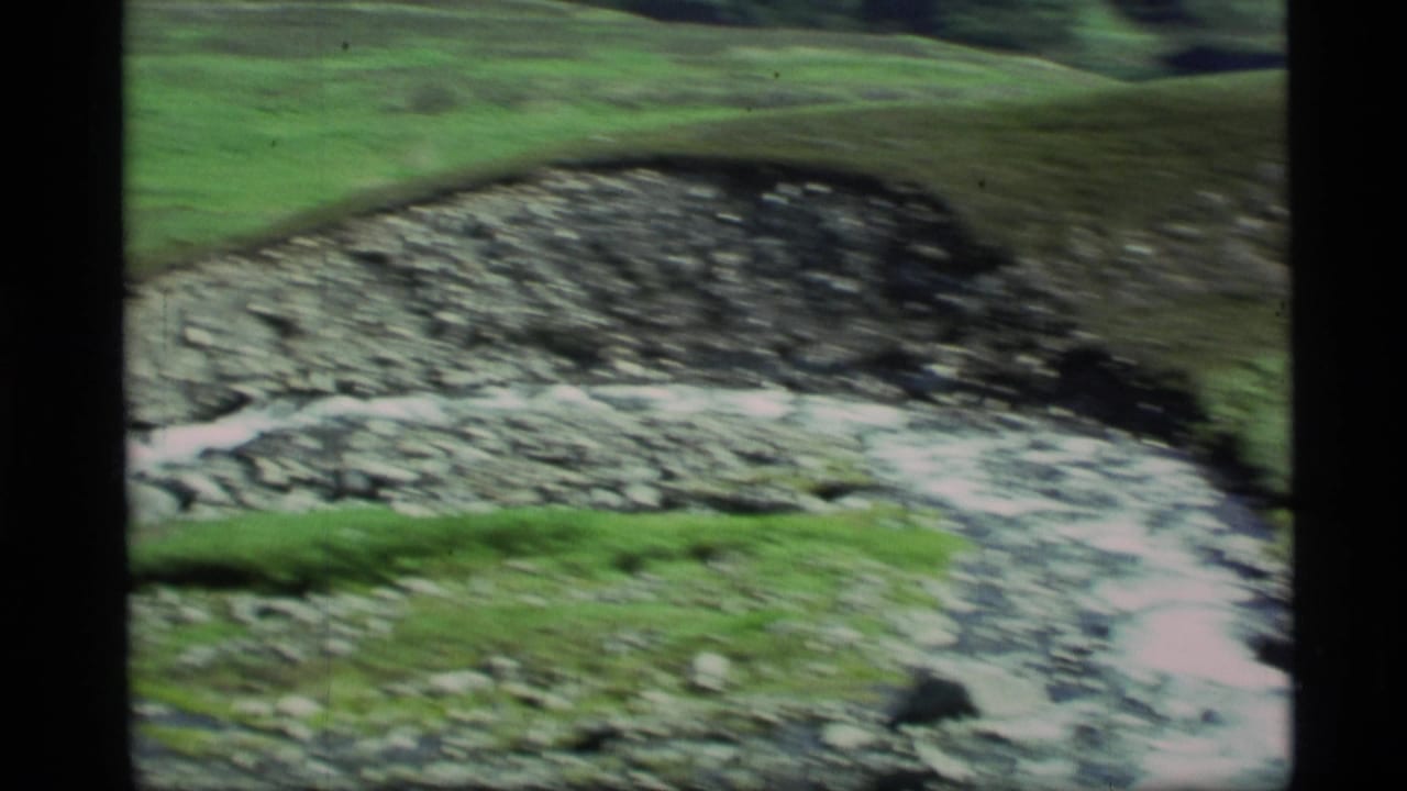 1977 Alaska 8mm frame showing a fast stream over rocks in a green mountain valley.