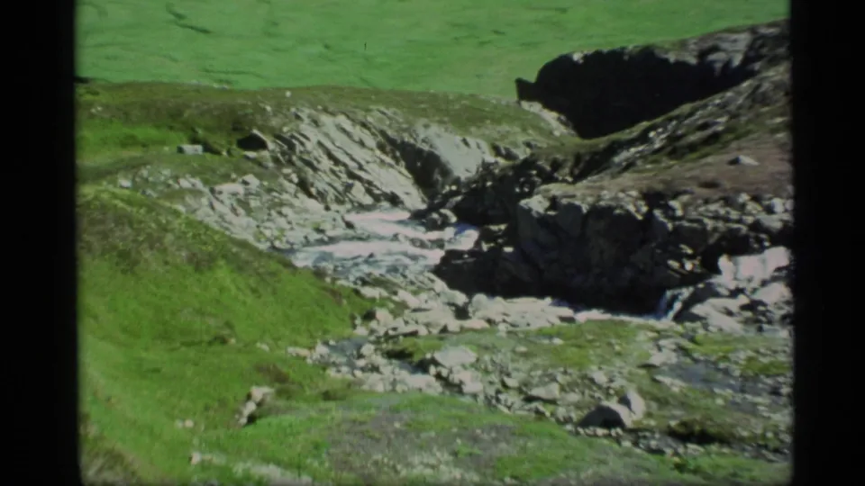 1977 Alaska 8mm view of a rocky creek winding through a bright green valley.