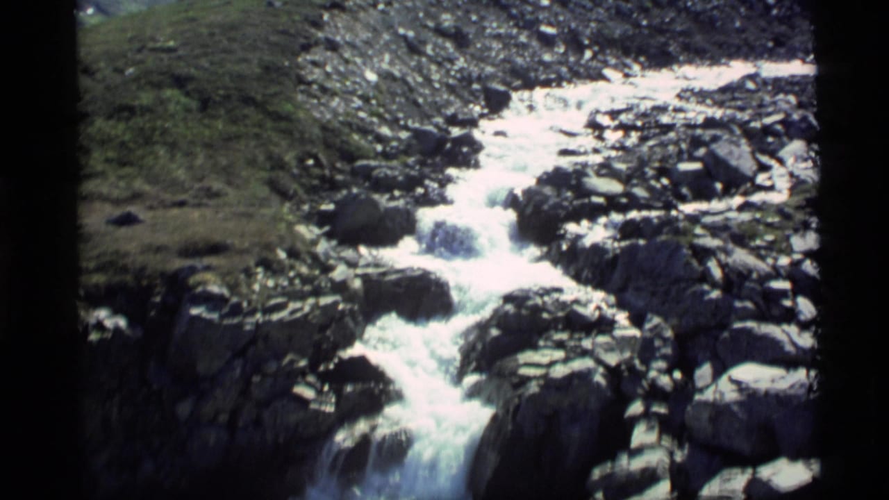 Whitewater stream descending through rocks on a grassy mountain slope.