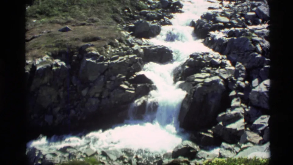 1977 Alaska 8mm still of bright whitewater cascading over boulders into a lower rocky pool.