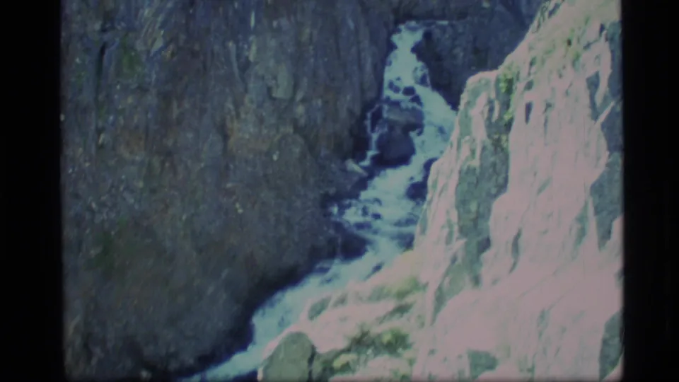 1977 Alaska 8mm frame of turbulent water curving past a bright rocky cliff and darker gorge wall.
