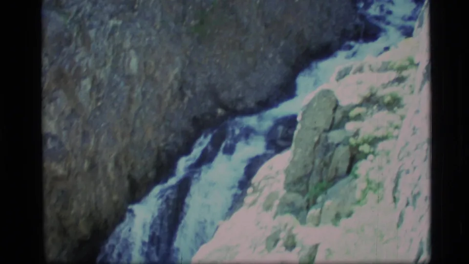 1977 Alaska 8mm frame of whitewater cascading past boulders and sheer pale rock in a mountain gorge.