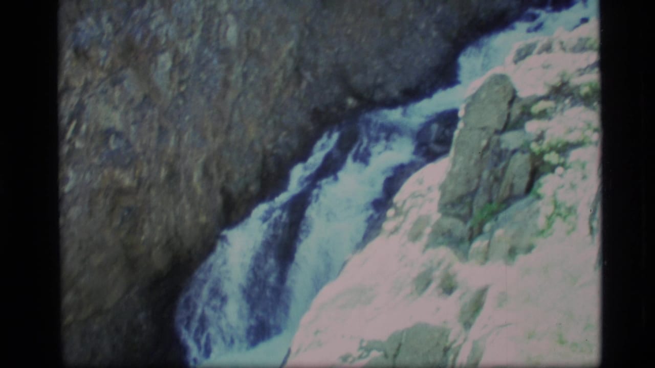 1977 Alaska 8mm frame showing white water dropping through a rocky canyon with bright sunlit stone at the edge.
