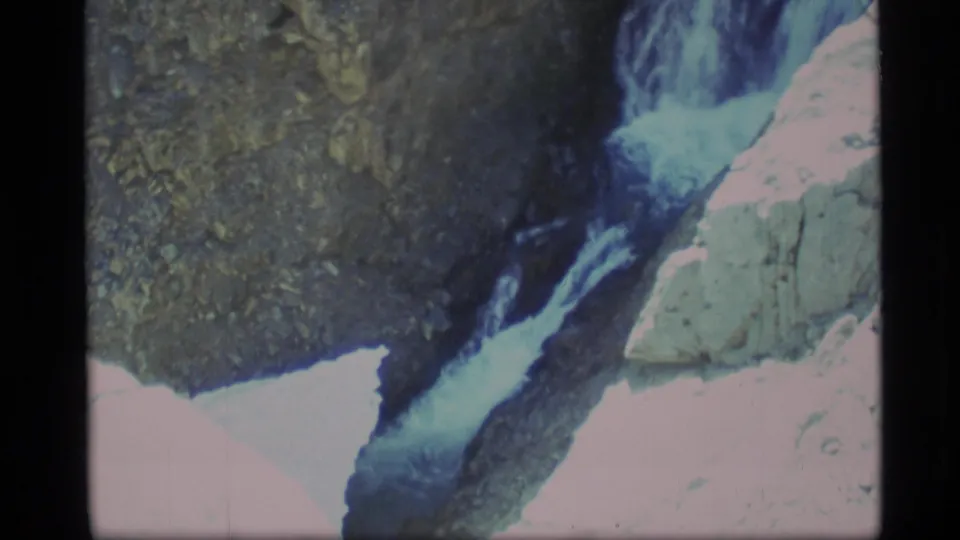 1977 Alaska frame showing the waterfall narrowing between dark canyon rock and a pale sunlit stone formation.