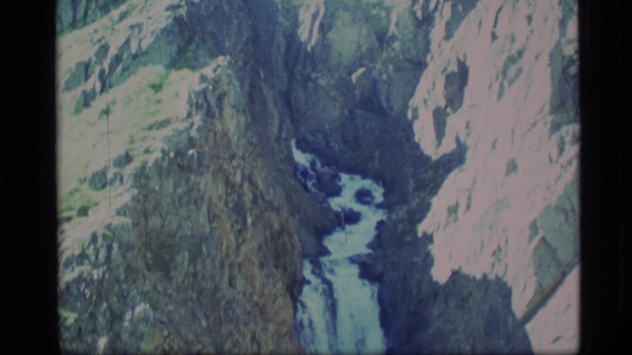 1977 Alaska 8mm frame showing a distant waterfall flowing through dark, rugged rock walls.