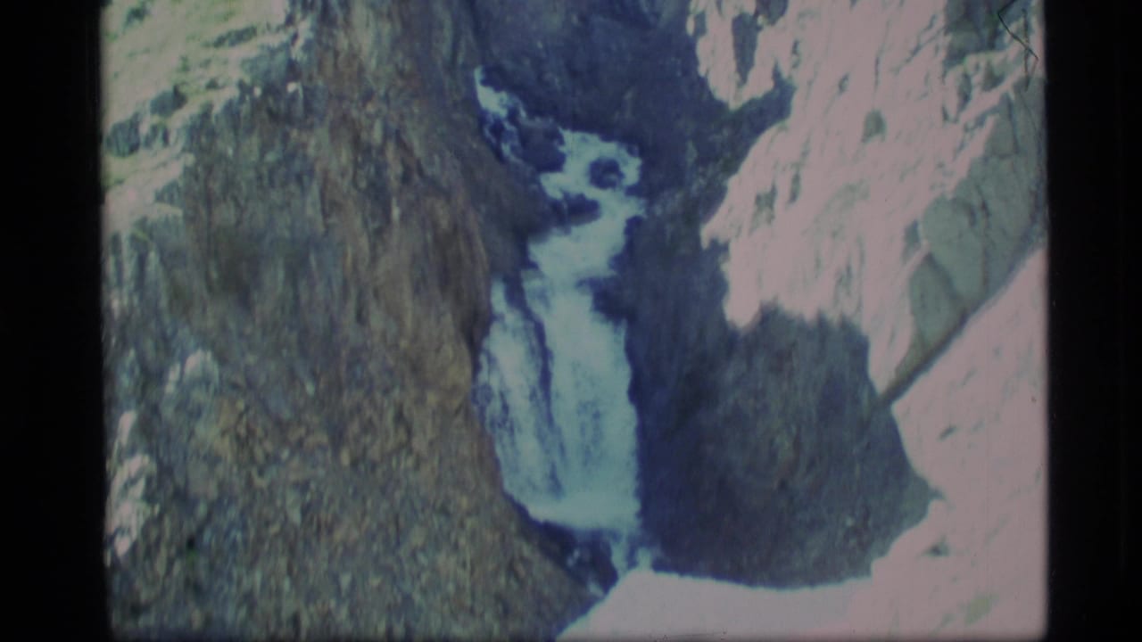 Waterfall and stream viewed between pale and dark rock faces.