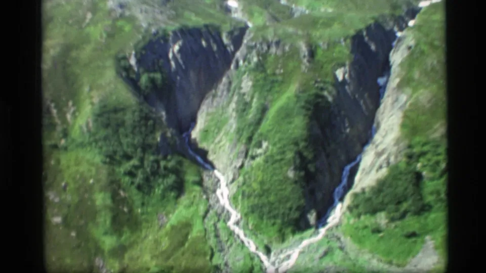1977 Alaska 8mm view looking into a steep green canyon with a narrow light-colored stream below.