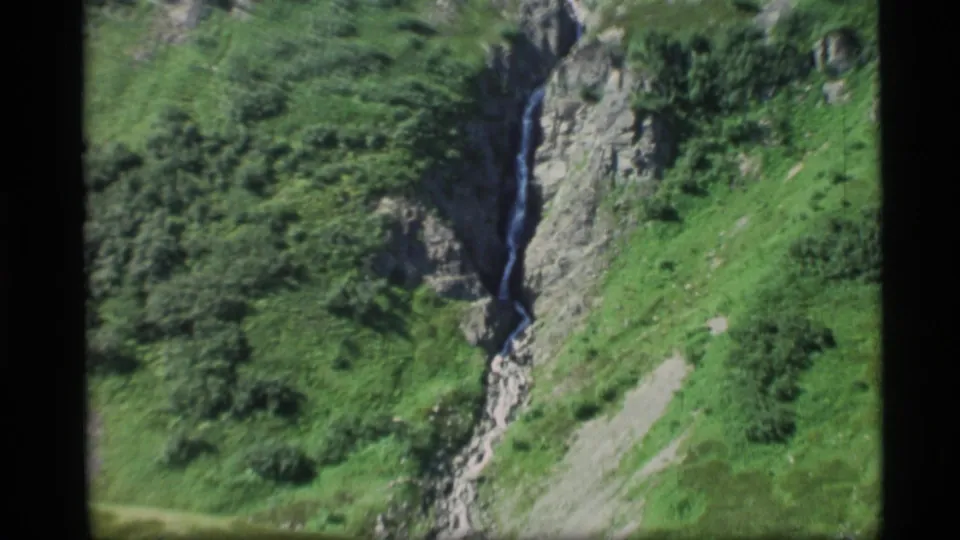 1977 Alaska 8mm view of a small stream winding down a rugged, grass-covered mountain slope.