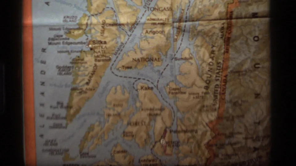 1977 8mm frame showing a closer section of the Alaska coastal map with islands, waterways, printed labels, and border text.