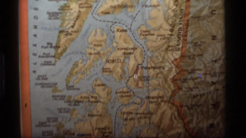 1977 8mm frame of a printed Alaska coastal map, including island names, shoreline labels, waterways, and the paper fold.