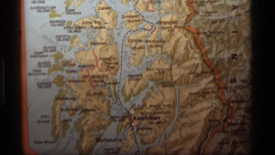 Final 8mm frame holds on the Alaska map, with labeled islands, blue channels, shaded mountains, and faded home-movie color.