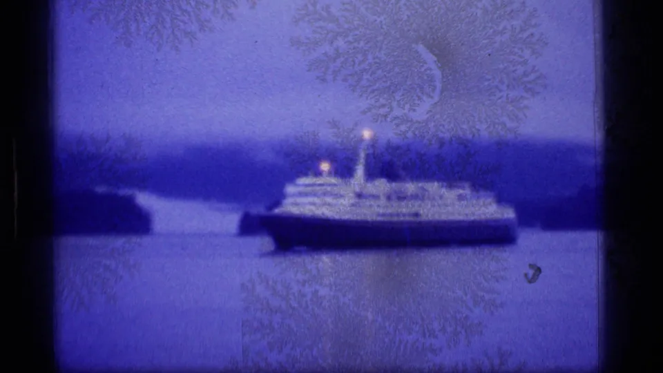 1977 Alaska home-movie frame of a passenger ship near shore, with mountains, water, and heavy blue film staining visible.