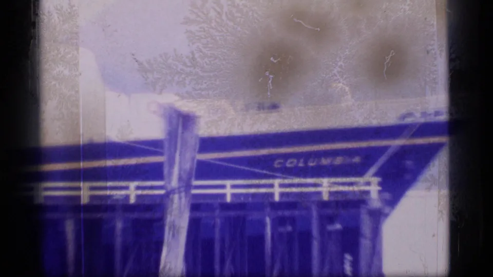 Dockside 1977 Alaska frame showing the Columbia name on a ship hull, with railings, pilings, and film wear across the frame.