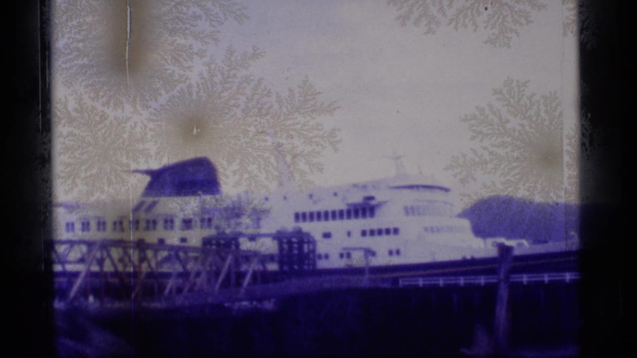 1977 Alaska home-movie frame of a white cruise ship at port, partly obscured by dark window edges and frost-like patterns.
