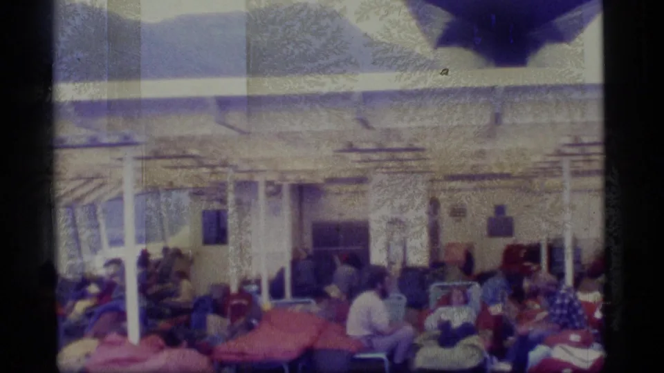 Passengers on a 1977 Alaska cruise deck sit and recline under posts and awning shadows in soft, faded 8mm footage.