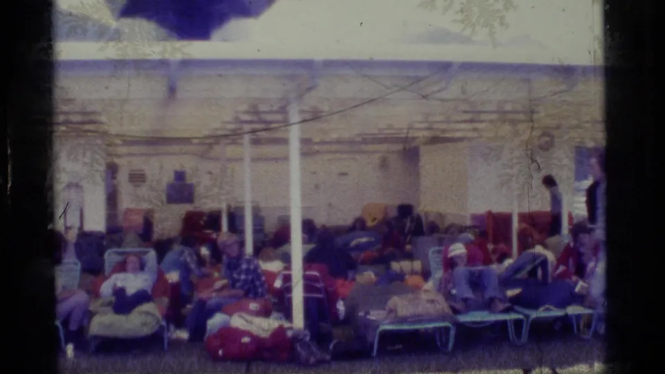 A wide home-movie view shows Alaska cruise passengers resting on deck chairs under a covered ship area in 1977.