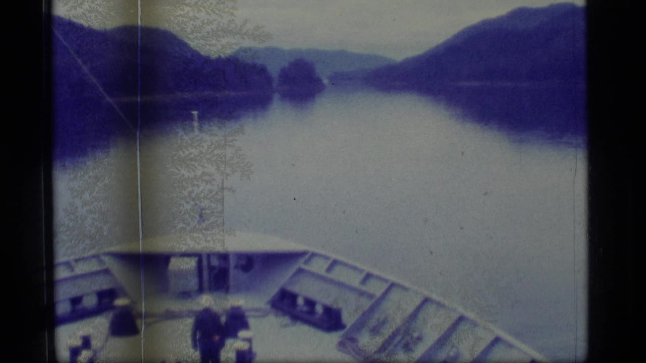 Vessel deck and bow facing a broad river or inlet with dark mountain slopes ahead.
